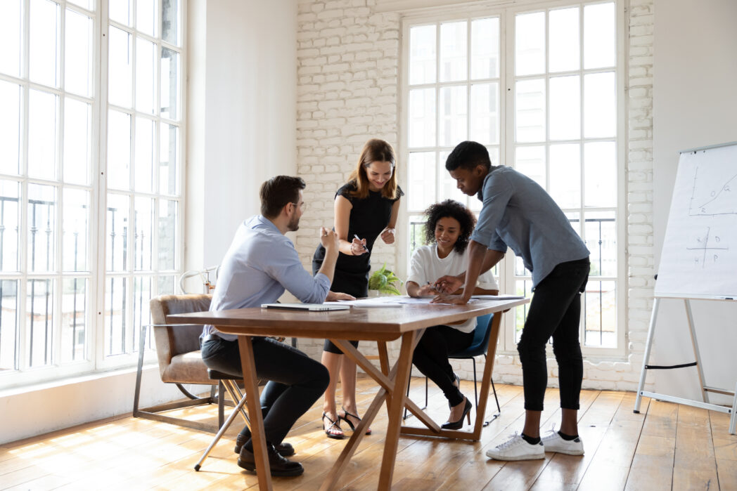 Motivated young diverse teammates working on project in office. Young creatives working on marketing projects gathered around a table.
