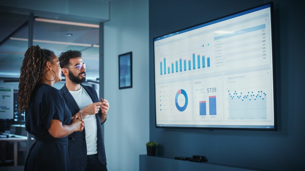 A highlight of key marketing trends - two workers looking a digital screen hanging on the wall showing analytics.